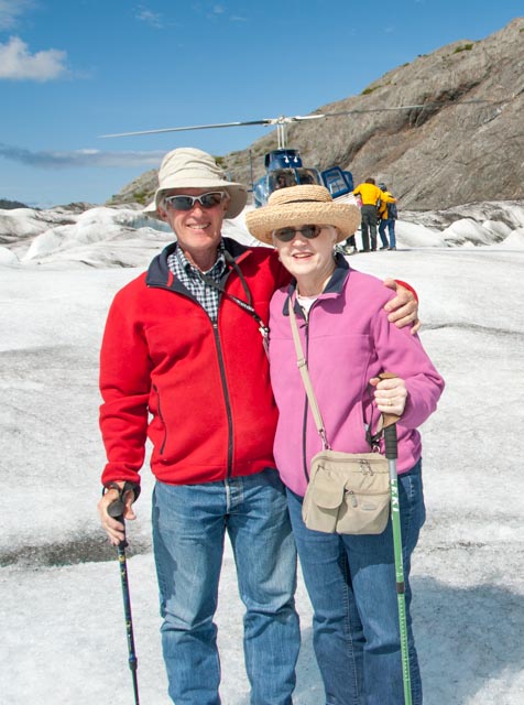 Dave and Marilyn sport big grins after a great helicopter trip to the glacier. What fun this is! In the background, the tour crew help previous visitors board for their flight back to Homer.